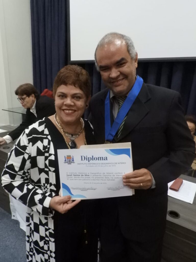 Juceli Santos e o Prof° Dr° Rui Aniceto Nascimento Fernandes posam para a foto com ambos segurando diploma de membro titular de Juceli.